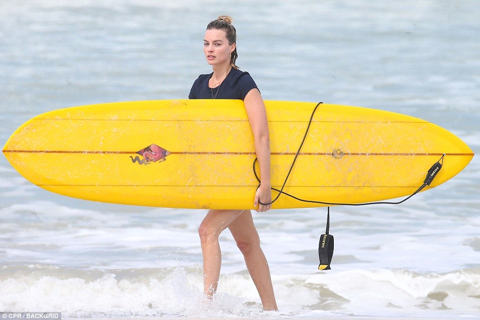 Golden girl: Margot carries her surfboard as she steps out the waves in Costa Rica 