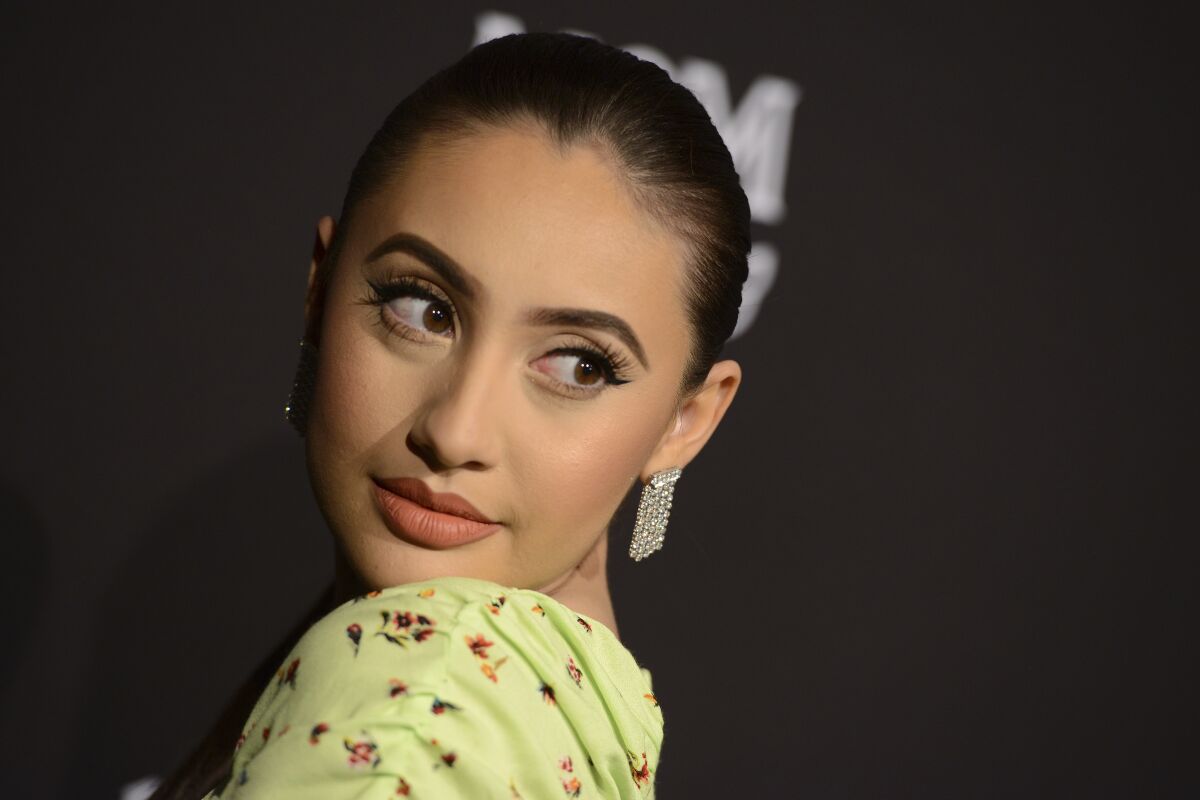 Francia Raísa poses in a green floral outfit and dangly earrings.